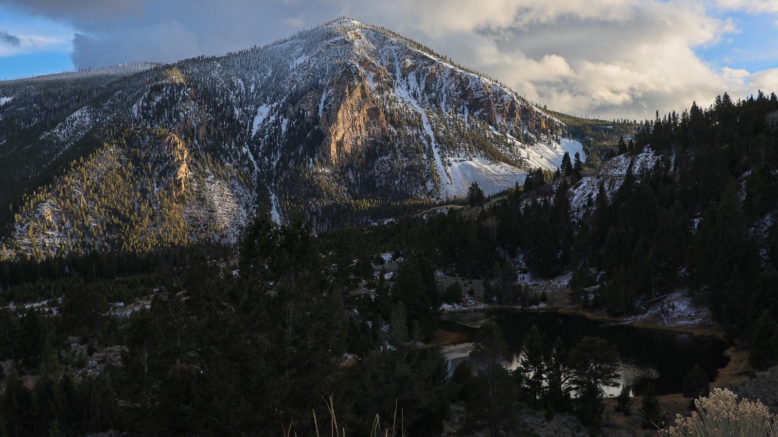 Golden hour light illuminates a small, rocky mountain with a small lake at the base of it.