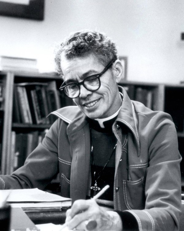 A portrait photograph of Pauli Murray seated at a desk with pen in her hand.