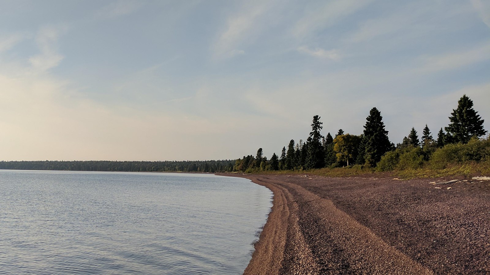 Lake Superior shoreline meets a rocky beach with trees in the distance.