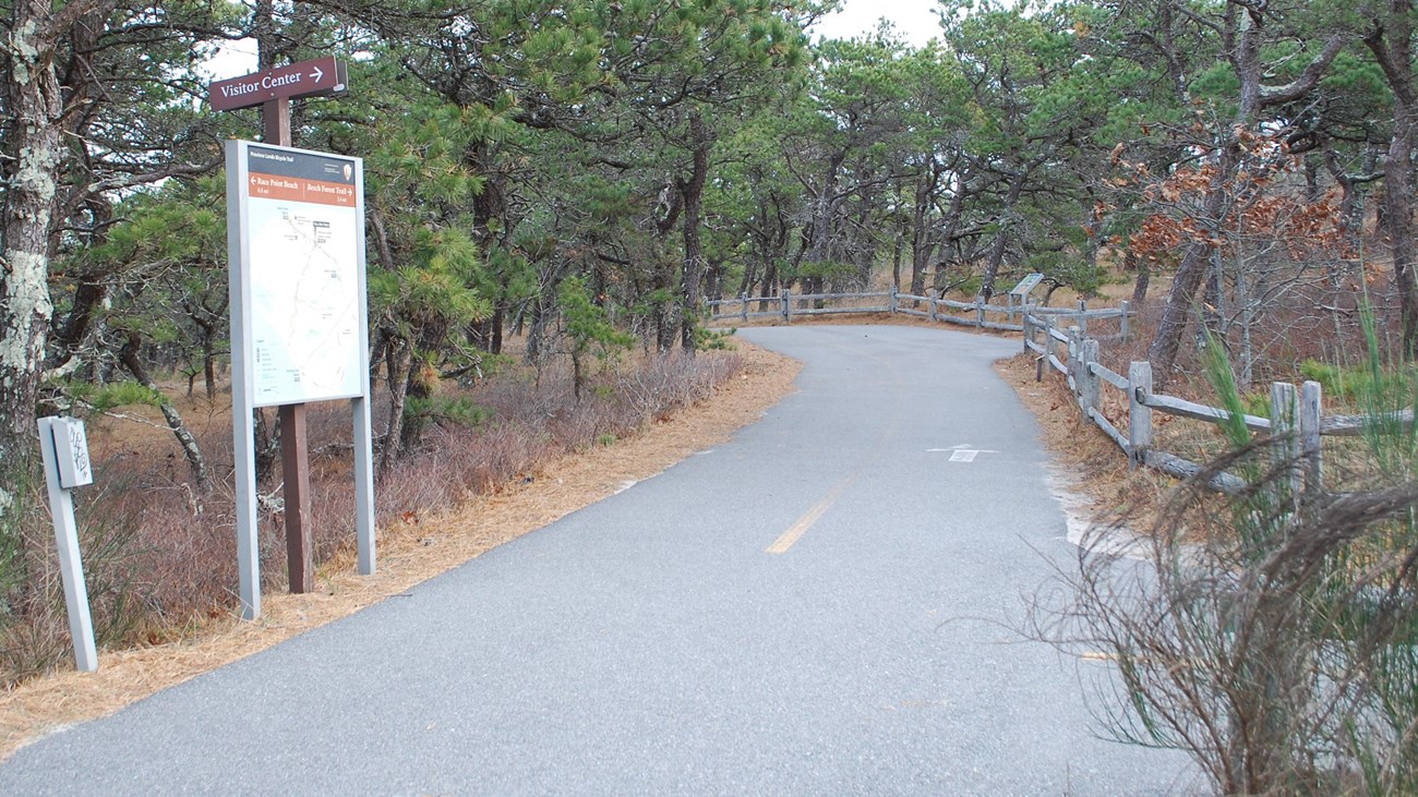 Entrance to the paved bike trail with regulation signage and trees.