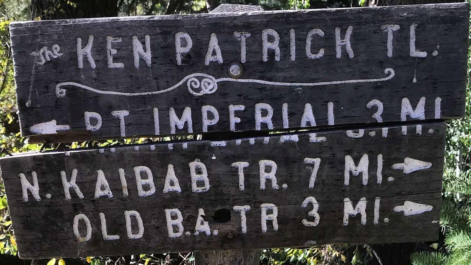 An old wooden sign with carved letters provides mileages and directions for the trail