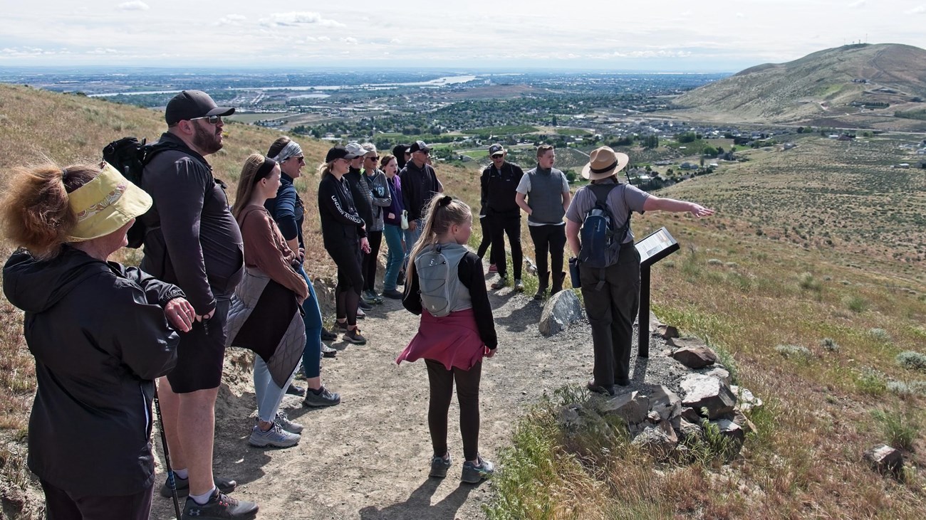 A group of people stand around a uniformed ranger pointing into the distance.