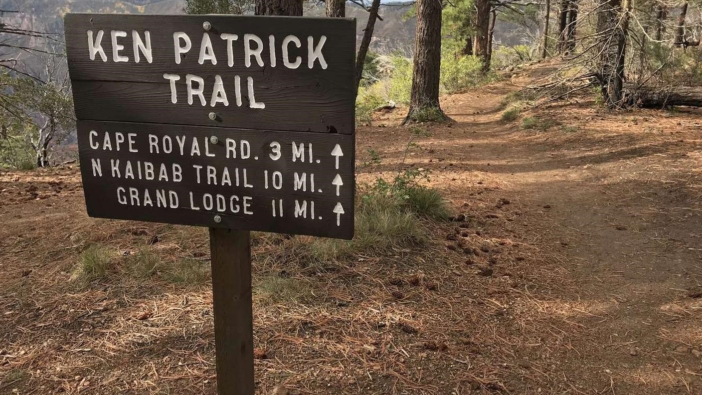 A wooden sign with white letters provides trail information next to a dirt path