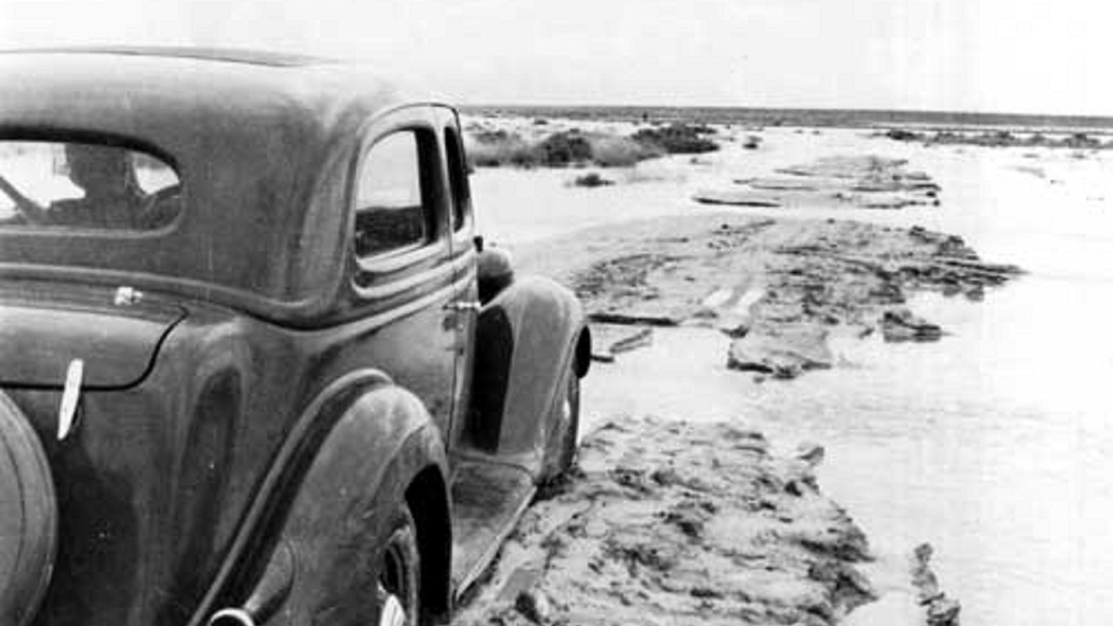 A vehicle from the 1940s driving on a washed out portion of White Sands\' old clay road.