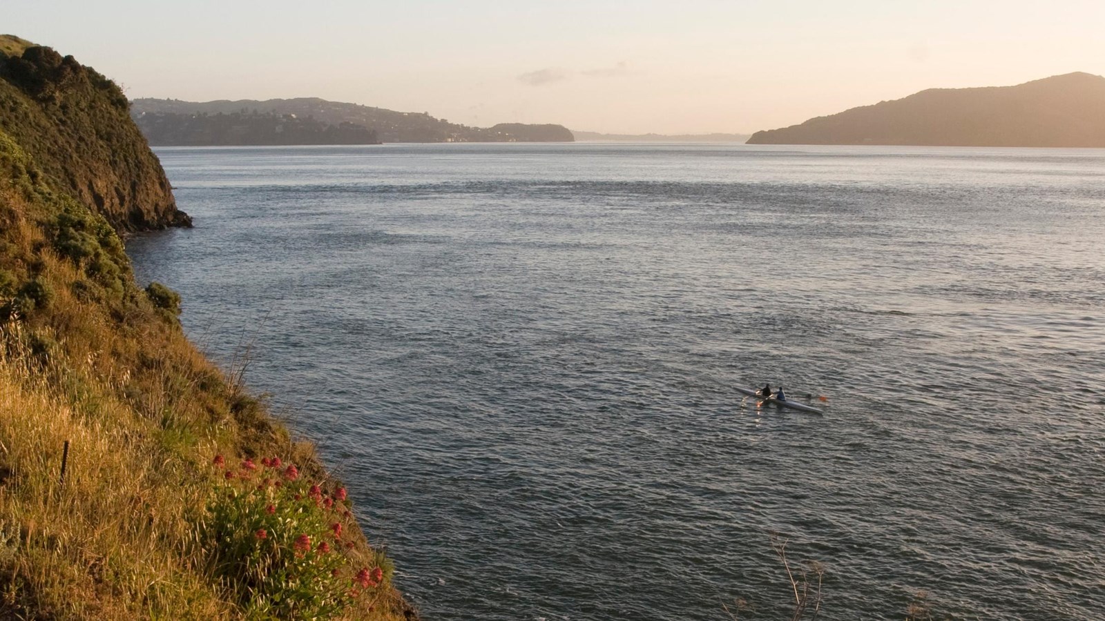 The grass covered cliffs overlooking the bay as kayakers pass by