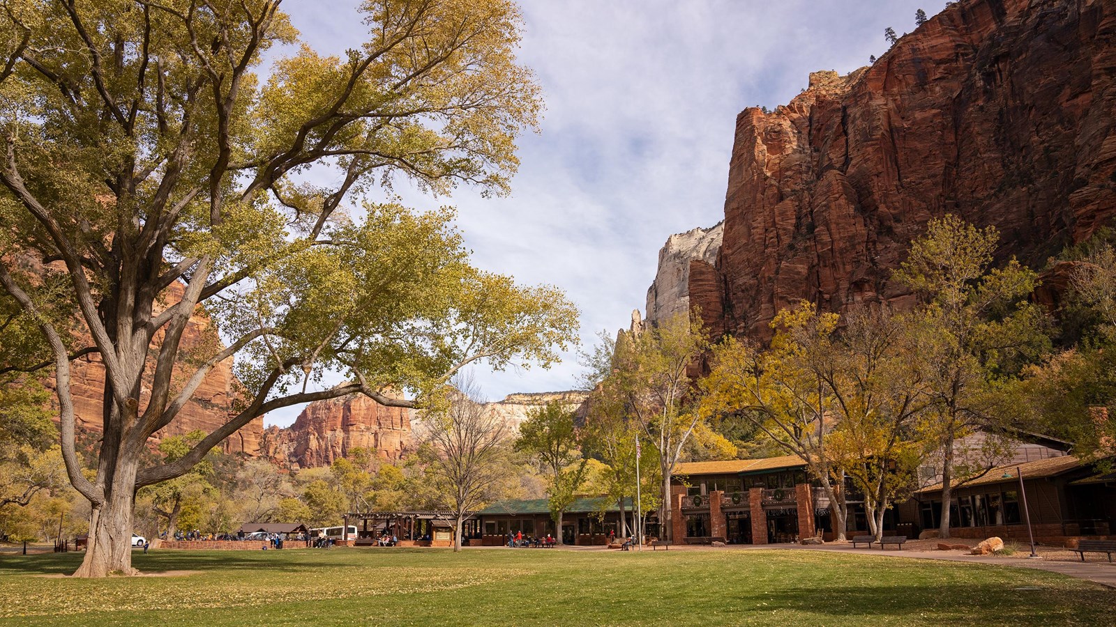 Photo of a brown building with a large grassy lawn in front of it, and mountains behind.