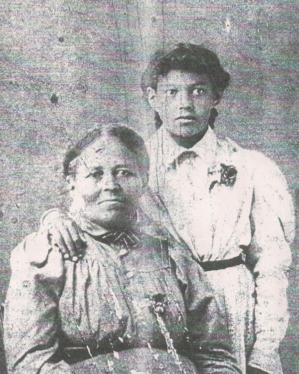 Faded black and white photo of Mary seated with her granddaughter standing beside.