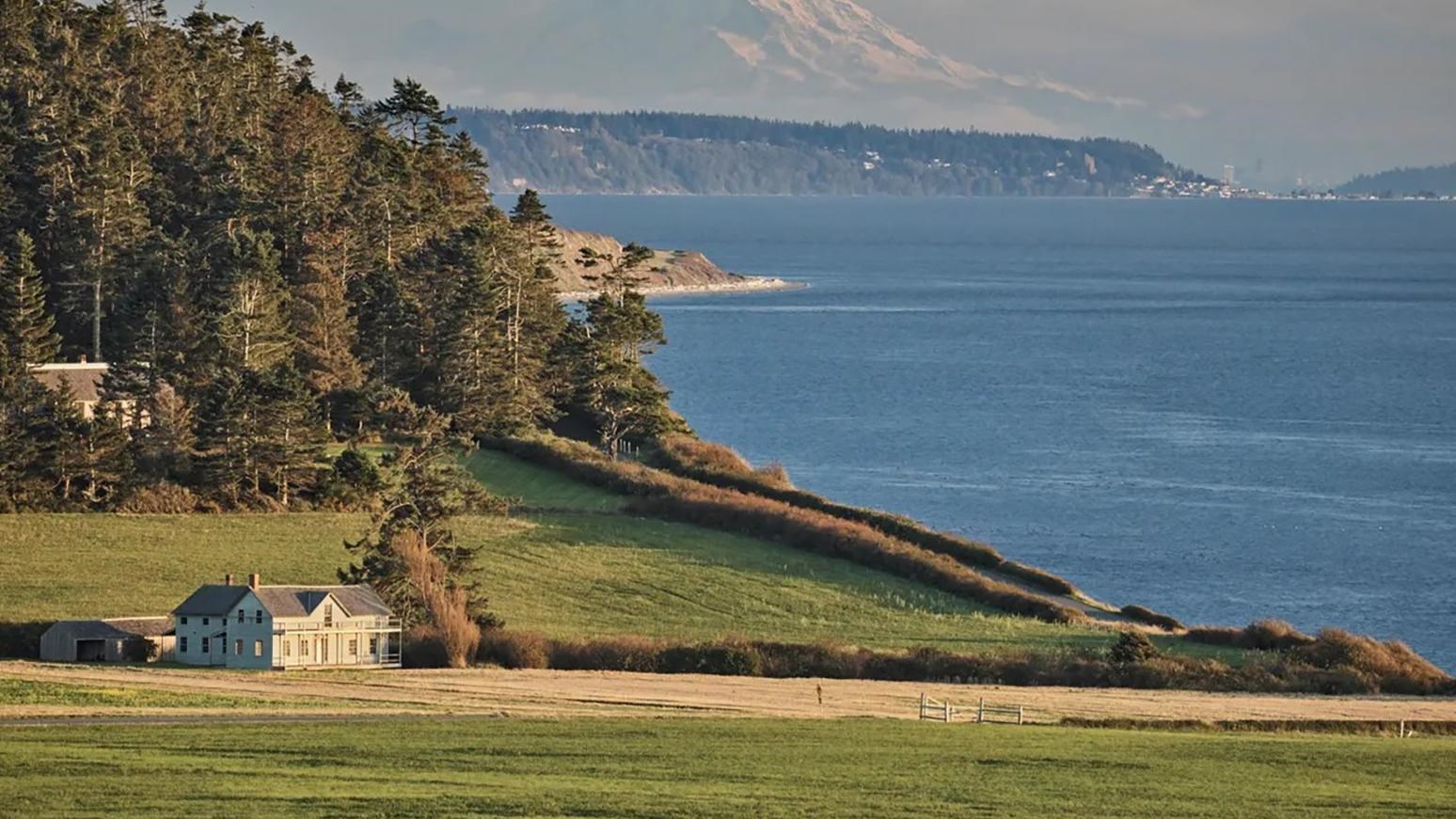 A historical house sits on a prairie near the ocean.