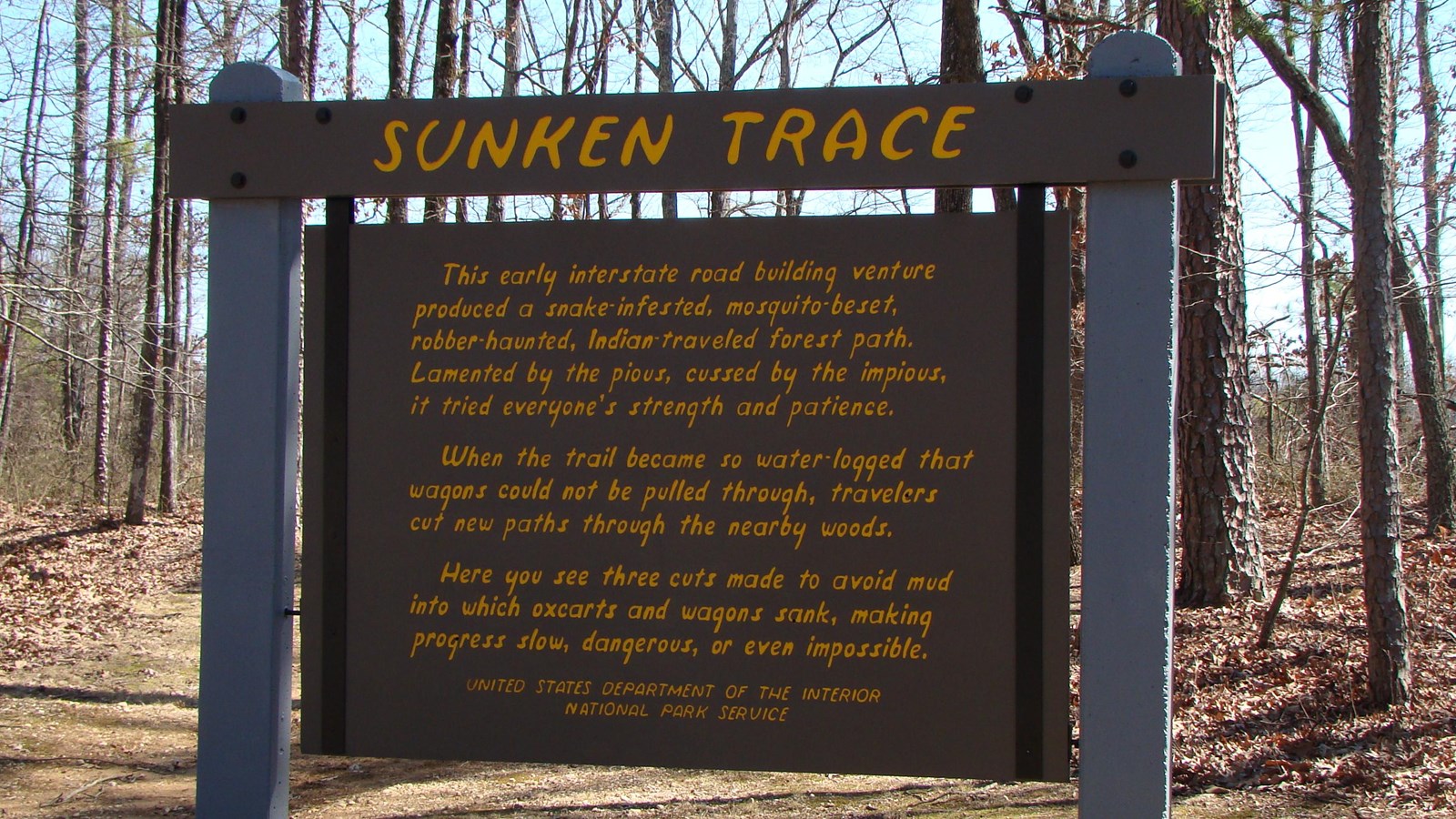 Wood sign painted brown with yellow letters, titled Sunken Trace