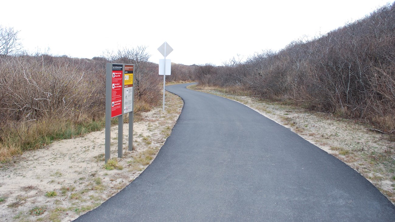 Entrance to the paved bike trail with regulation signage and bushes.