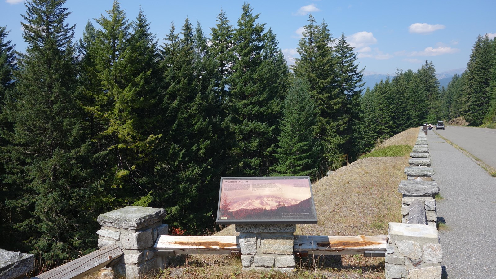 A wayside exhibit panel attached to a stone post along a fence next to a pullout.