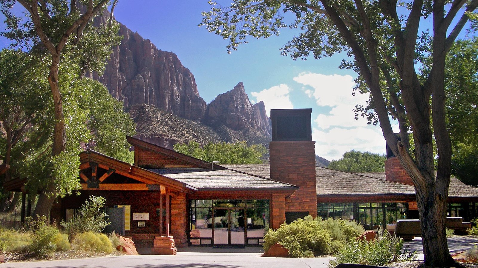Photo of a sandstone building under a cloudy blue sky, surrounded by green trees.