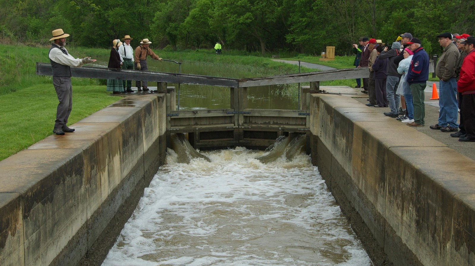 Four people in historic costume stand on the left side of a water-filled stone lock. 