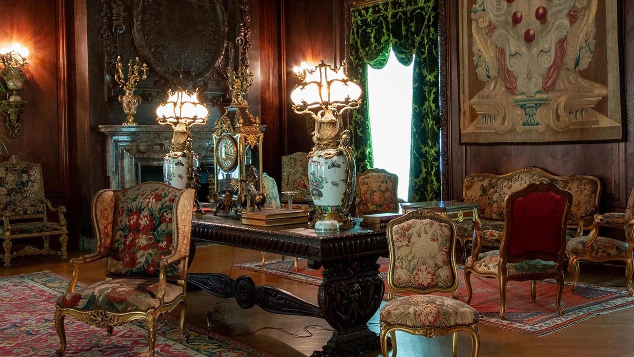 A large paneled room with a variety of furniture, carpets, and tapestries.