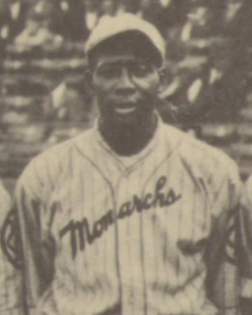 African American man stands in front of viewer wearing baseball uniform of the 1920s