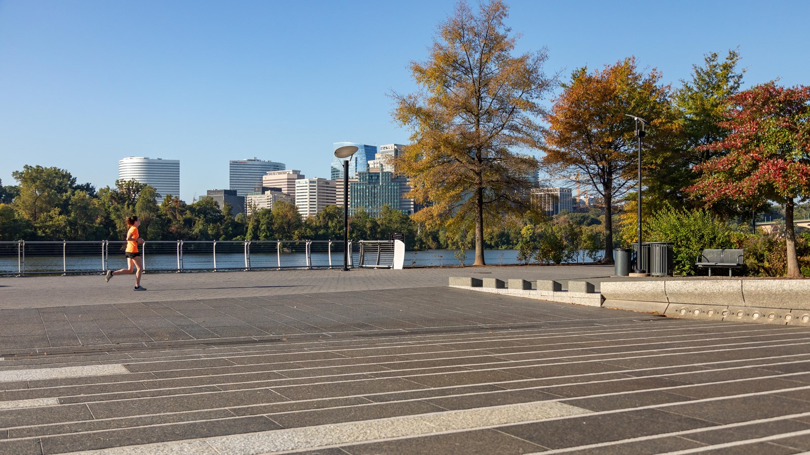 A stone plaza by the Potomac River flanked by colorful fall trees.