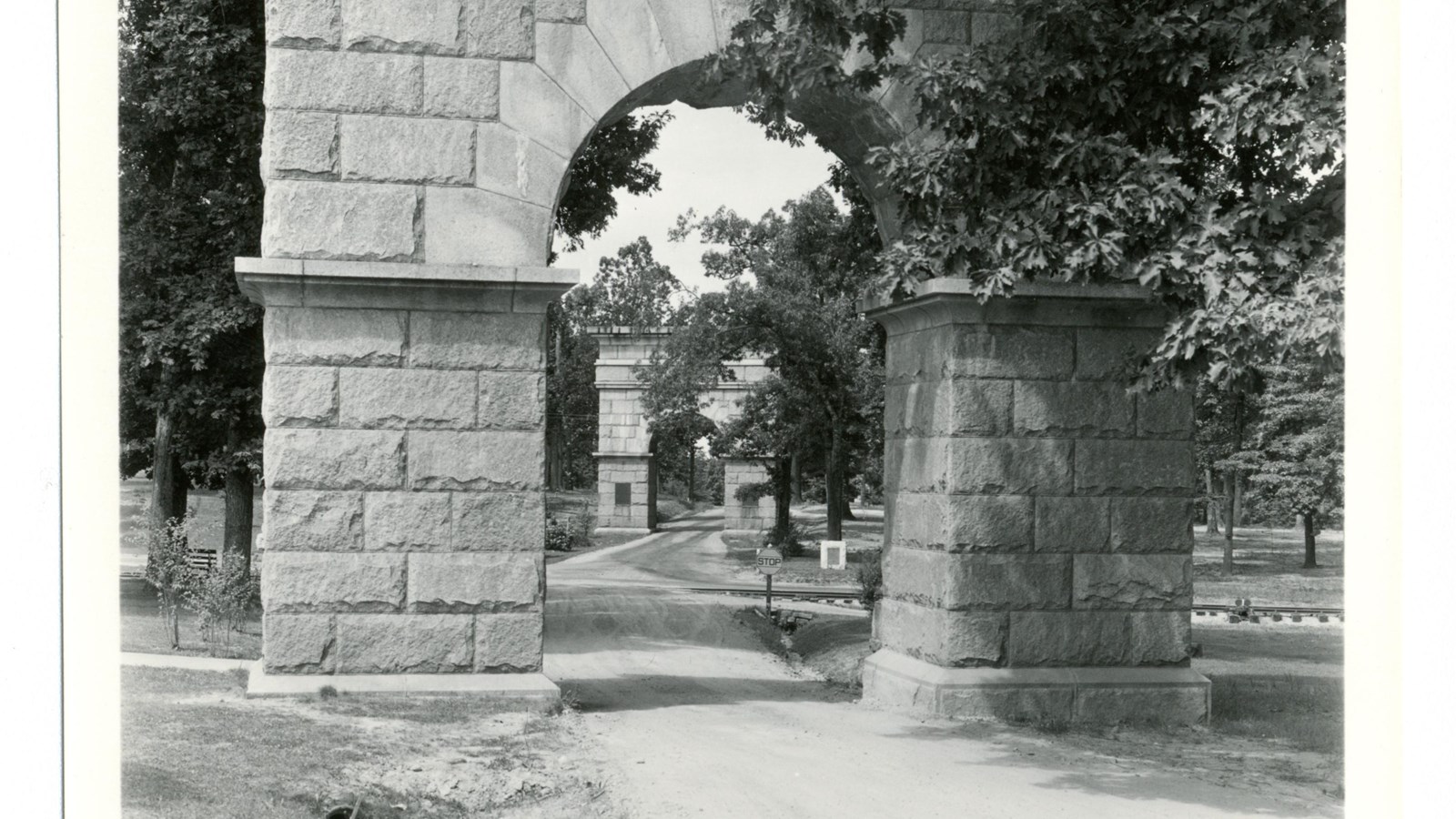 30 foot tall stone arches loom over a dirt road that pass under them.