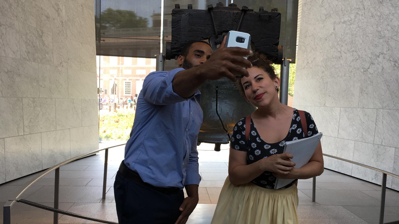 A man and a woman take a selfie photo in front of the Liberty Bell.