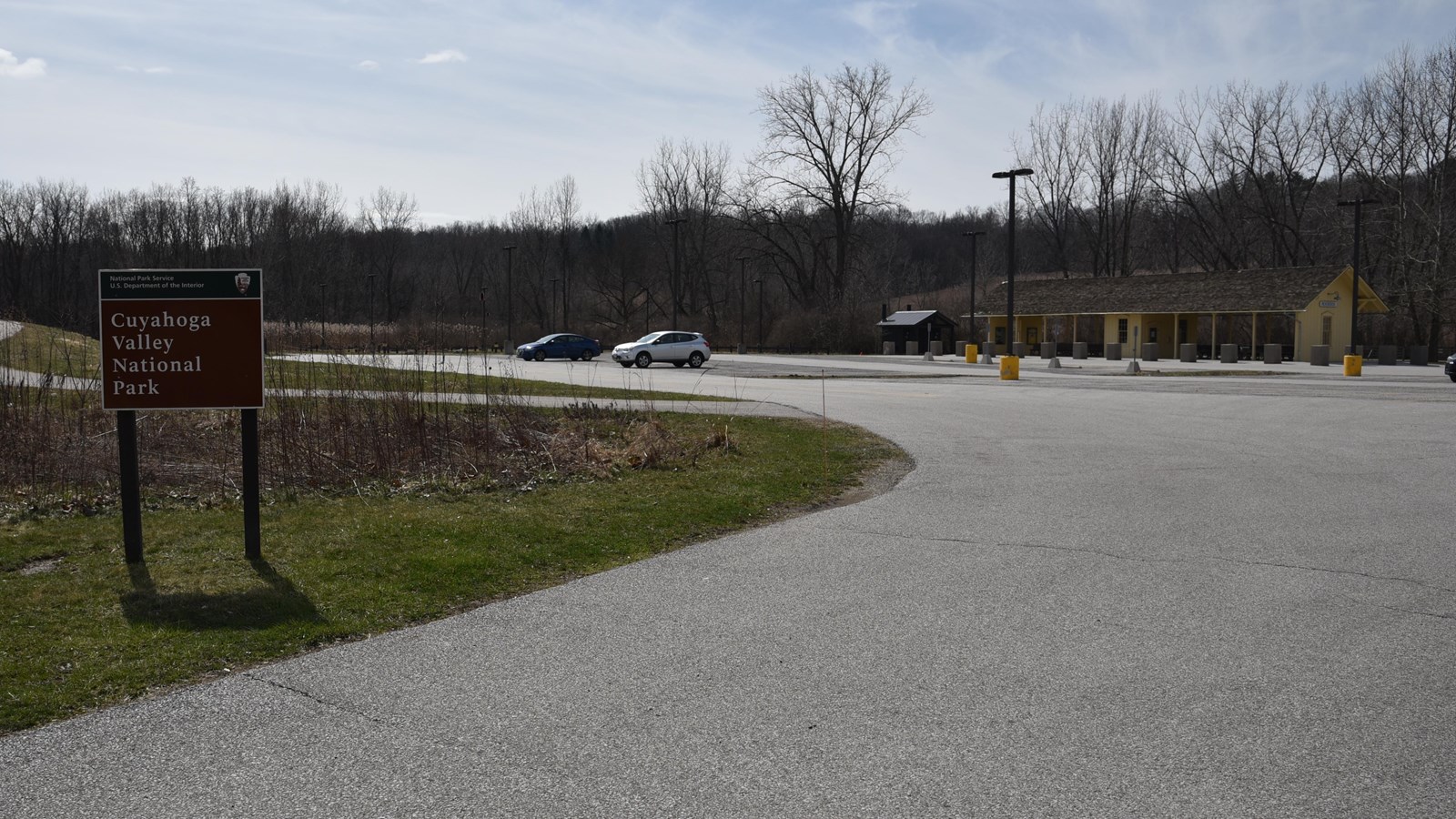 Park sign at the entrance to a large parking lot. On the right side is a yellow train station.