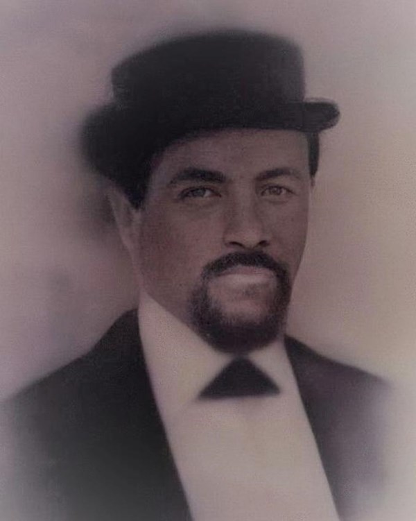 Portrait of a black man with goatee and fedora with black suit jacket and white dress shirt