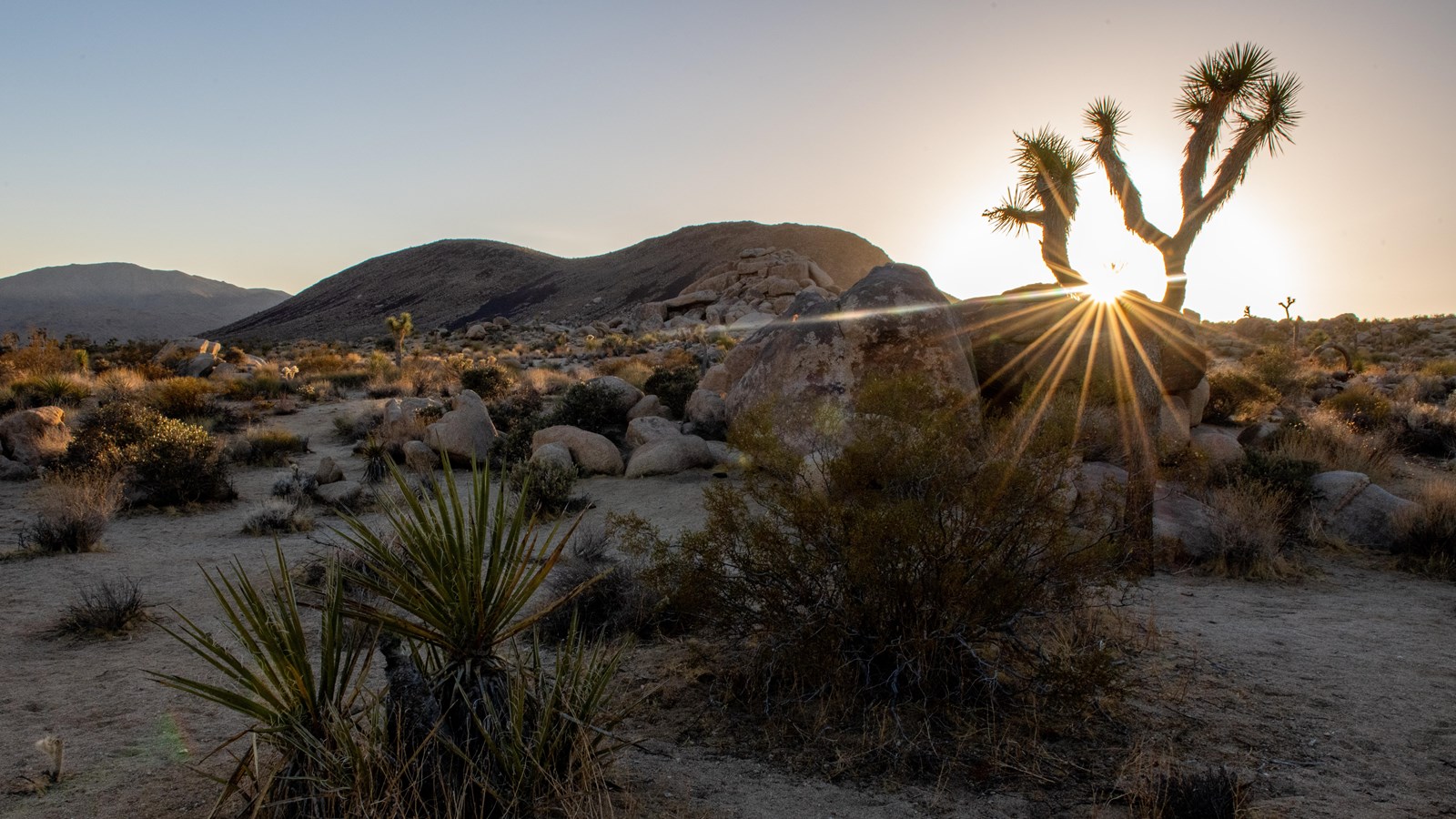 A sun setting behind a dark-colored hill 