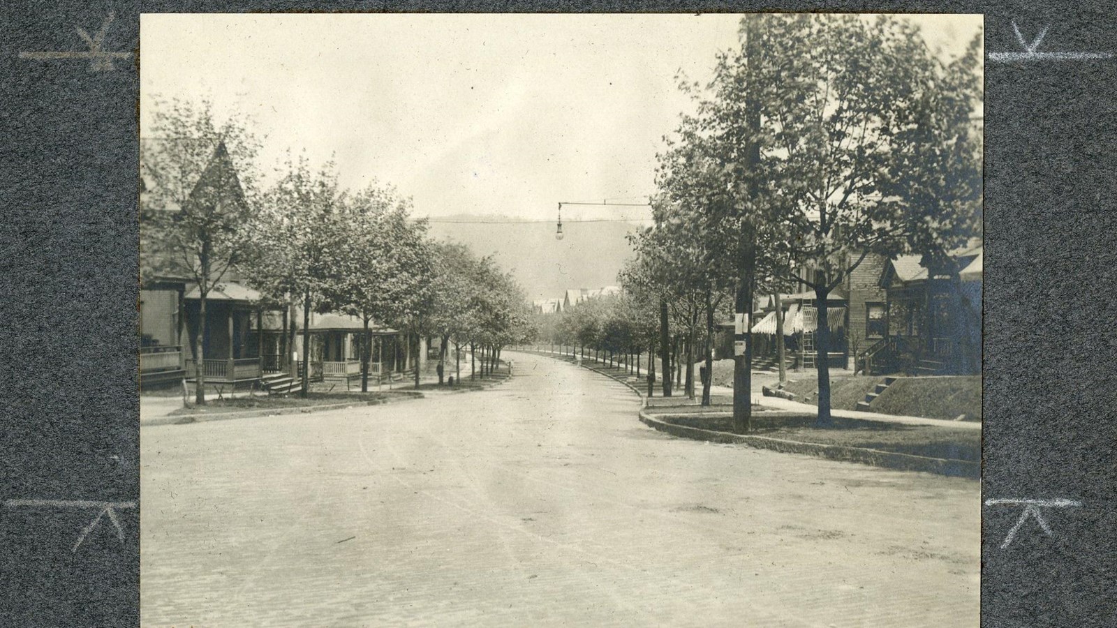 Black and white of curving road lined with trees on both sides along sidewalk with homes