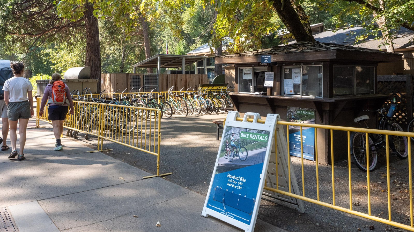Yellow metal fencing surrounds a fleet of bicycles and a small brown structure
