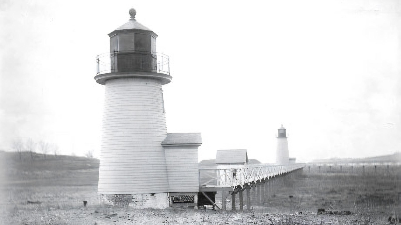 Black and white photo of a light station on a rocky beach. 