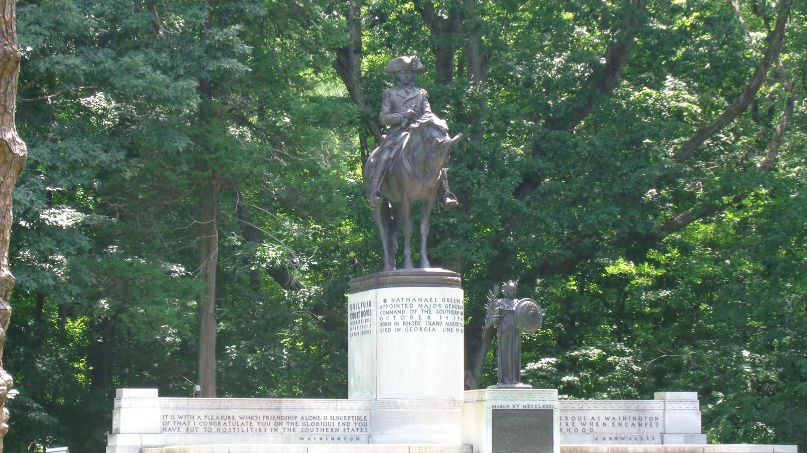 A larger than live statue of Greene on horseback atop a pedestal. Behind him is a lush forest.