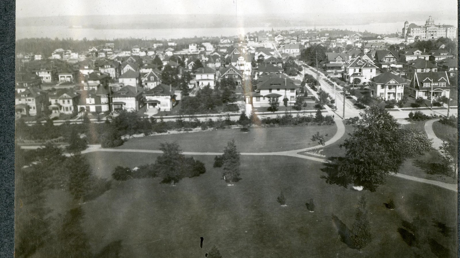 Black and white aerial of grassy area next to community with curving path, trees spread out on grass