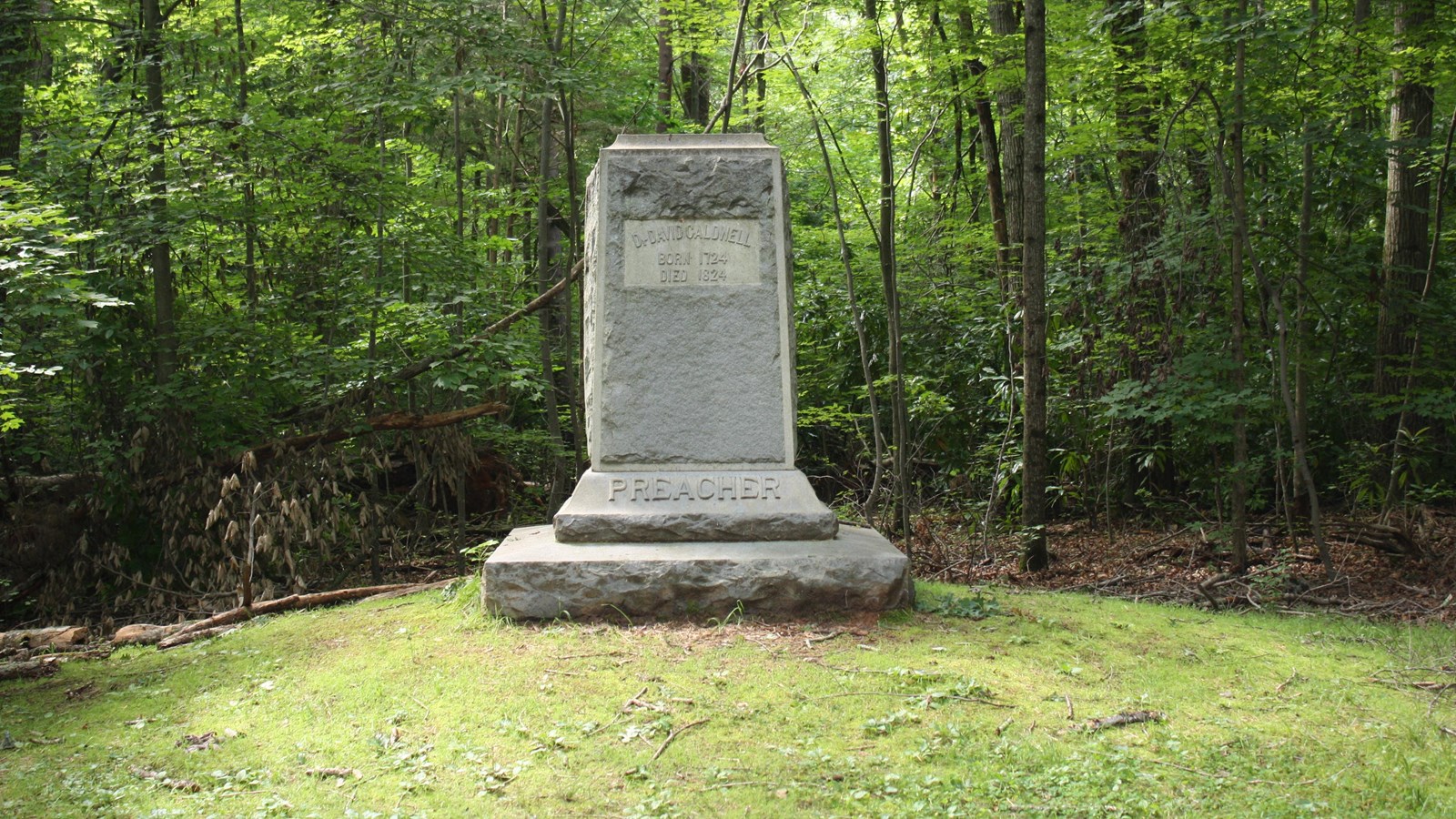A large rectangular stone with inscriptions sits nestled deep in the forest.