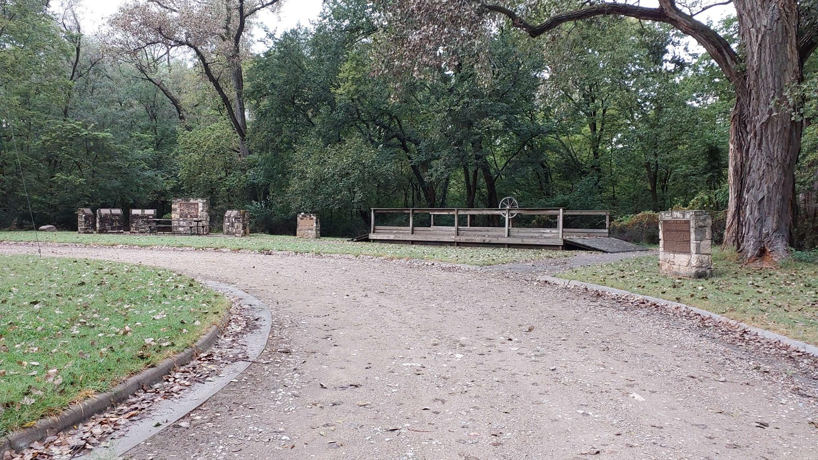 A road path leads to stone interpretive panels and a replica ferry to the right of the path.
