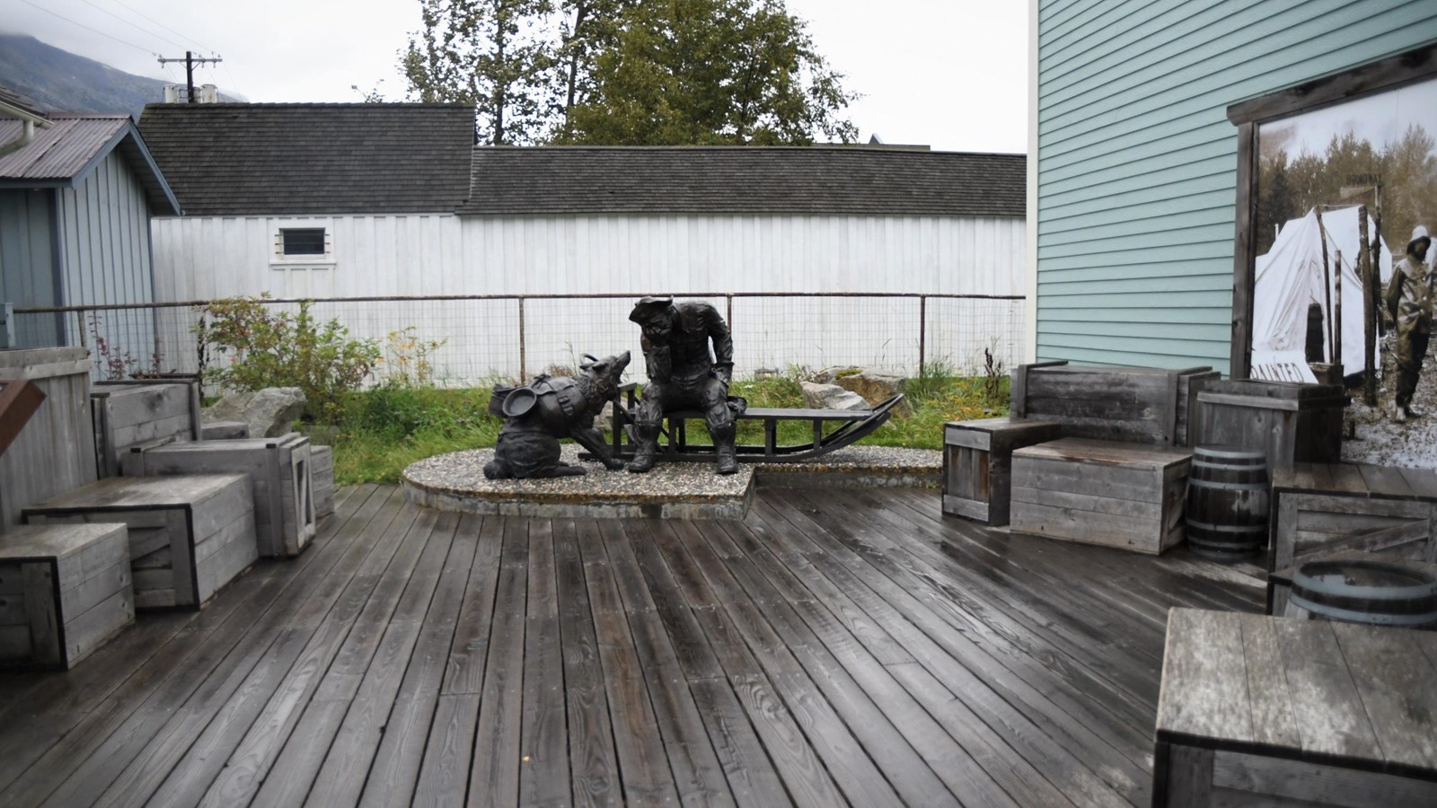 Metal sculpture of a tired man and his dog. Many wooden boxes are stacked around them.