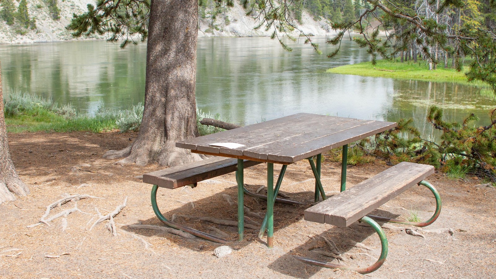 A picnic table in front of a river that is lined by trees