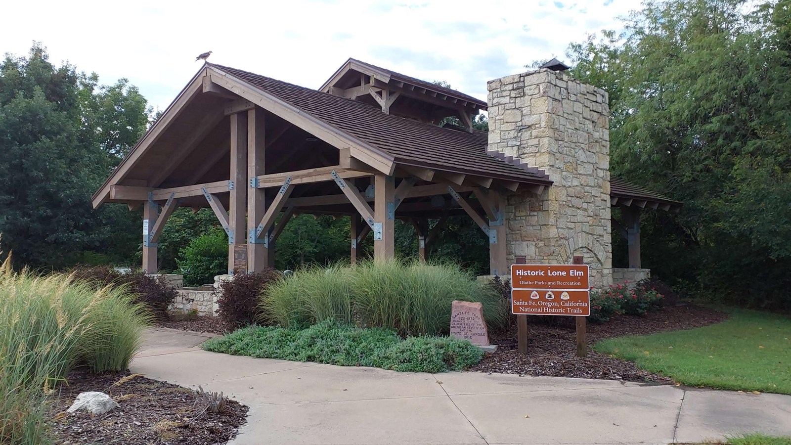 An entrance sign for Historic Lone Elm sits beside a covered wooden covered structure.