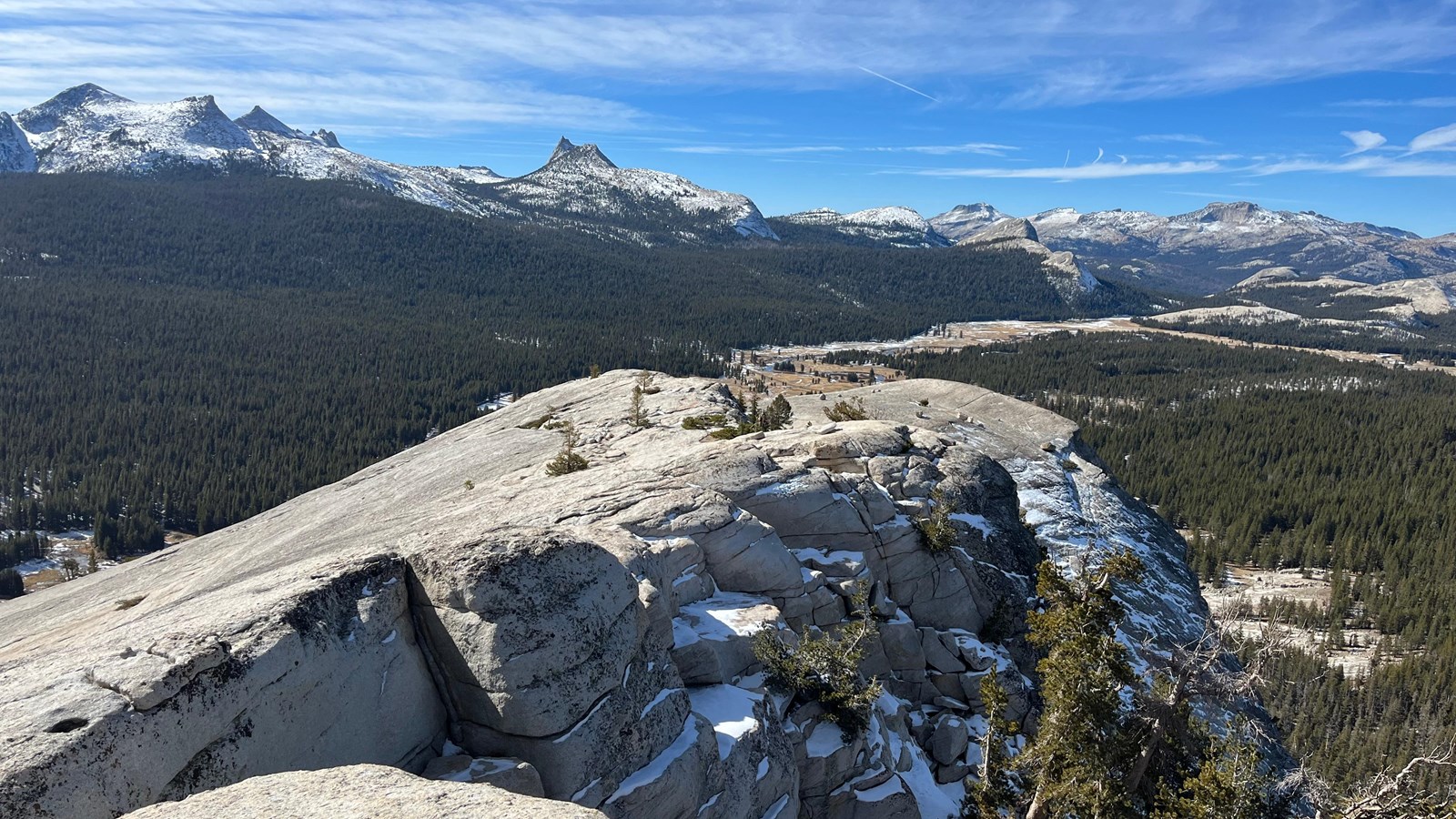 Bare rock in the foreground with snowy peaks and partly cloudy skies towering behind