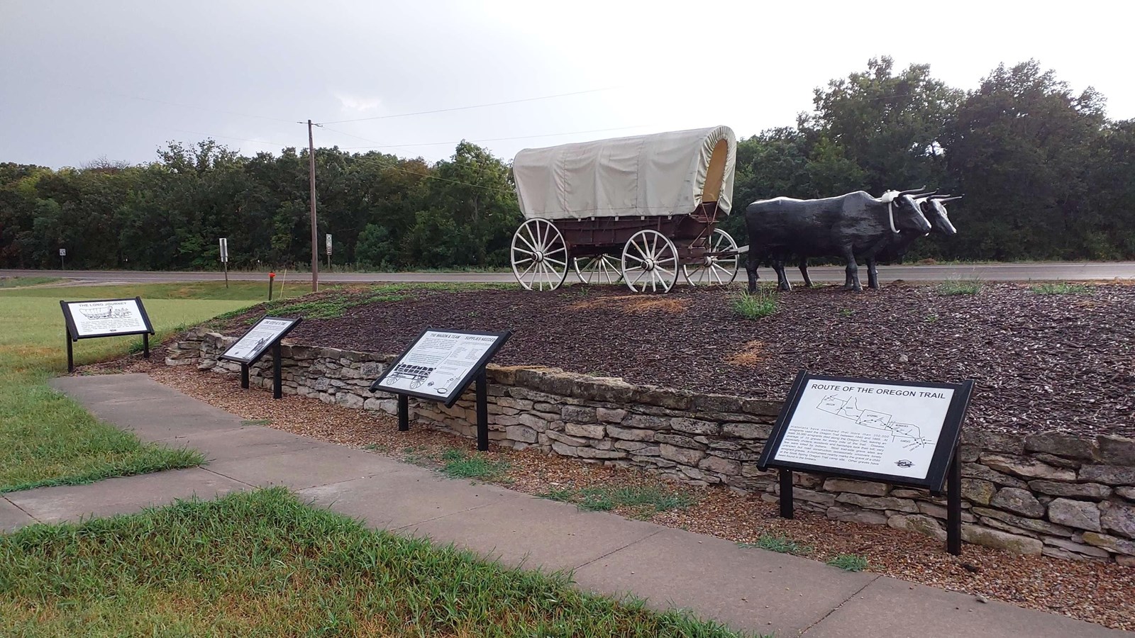 A short side walk with interpretive panels to the right is next to small hill with wagon.