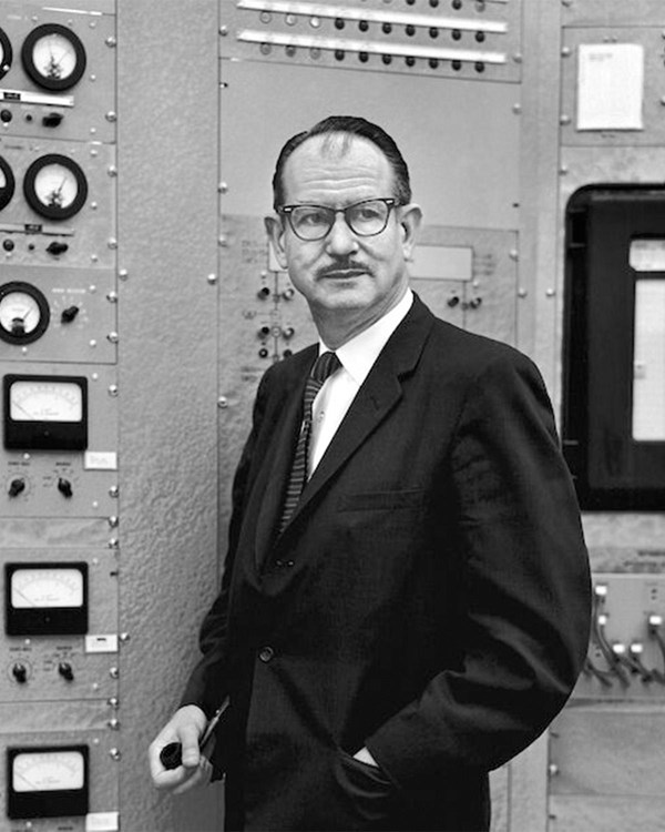 A man in a suit stands in front of scientific equipment.