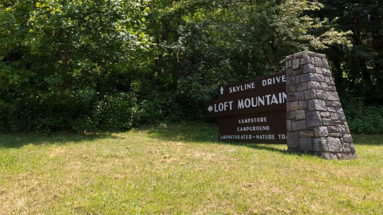A large brown sign with white letters is attached to a stone pillar on the right.