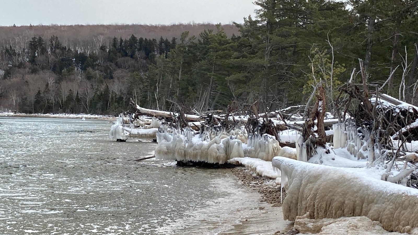 Icy spray-covered driftwood and logs on the beach next to partly-frozen Lake Superior.