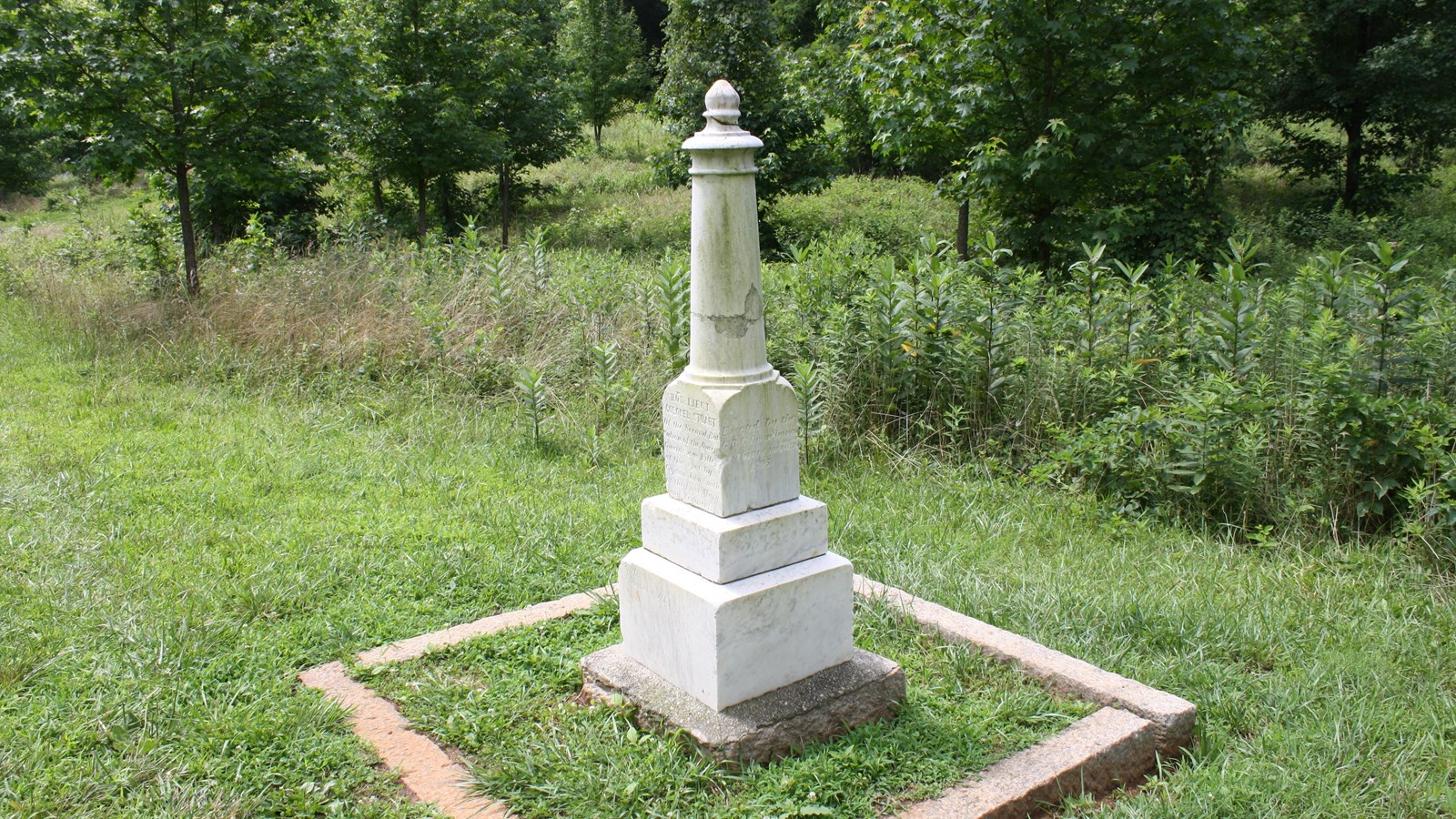 A short Georgian Marble cylindrical monument stands in a field. It sits on a tiered foundation.