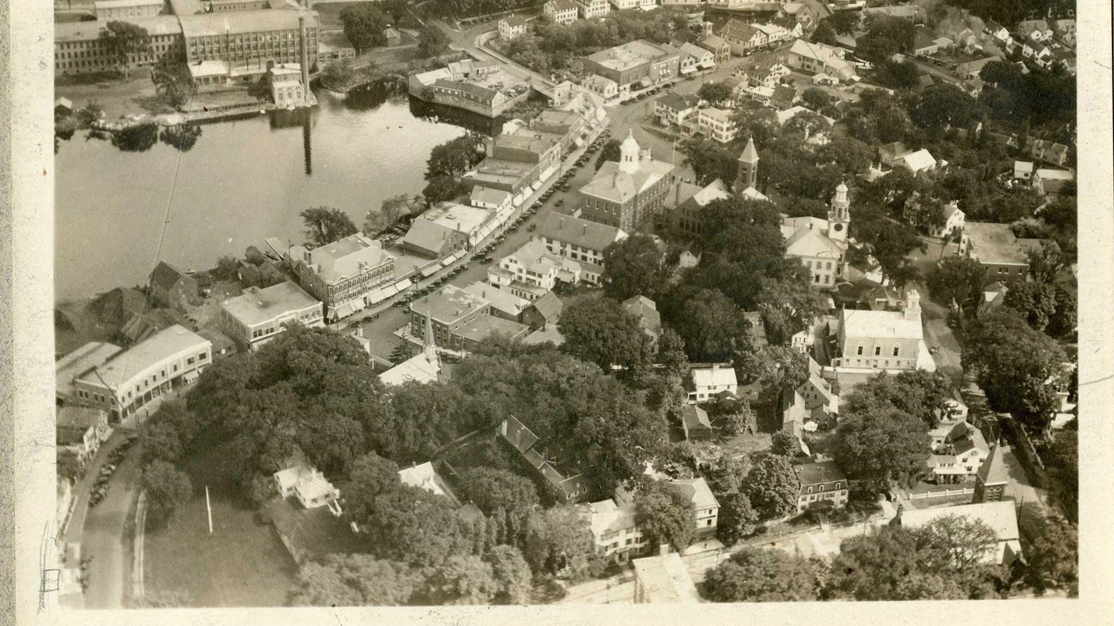 Black and white aerial of campus with buildings separated by trees, busy street on far edge