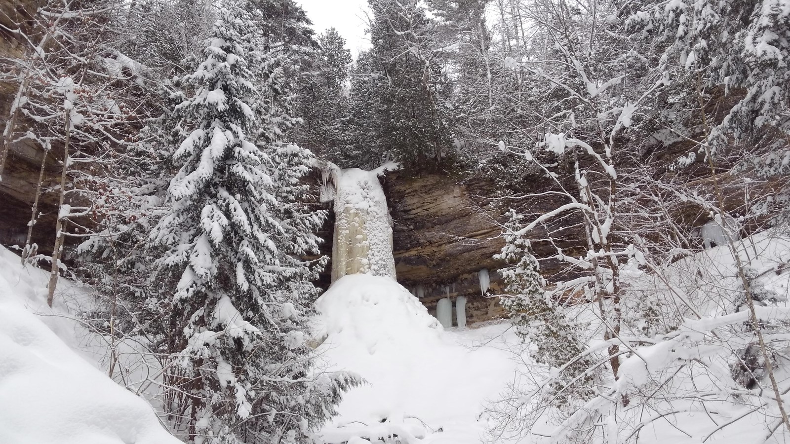 Waterfall encased in ice column dropping down from cliff in snow-covered canyon
