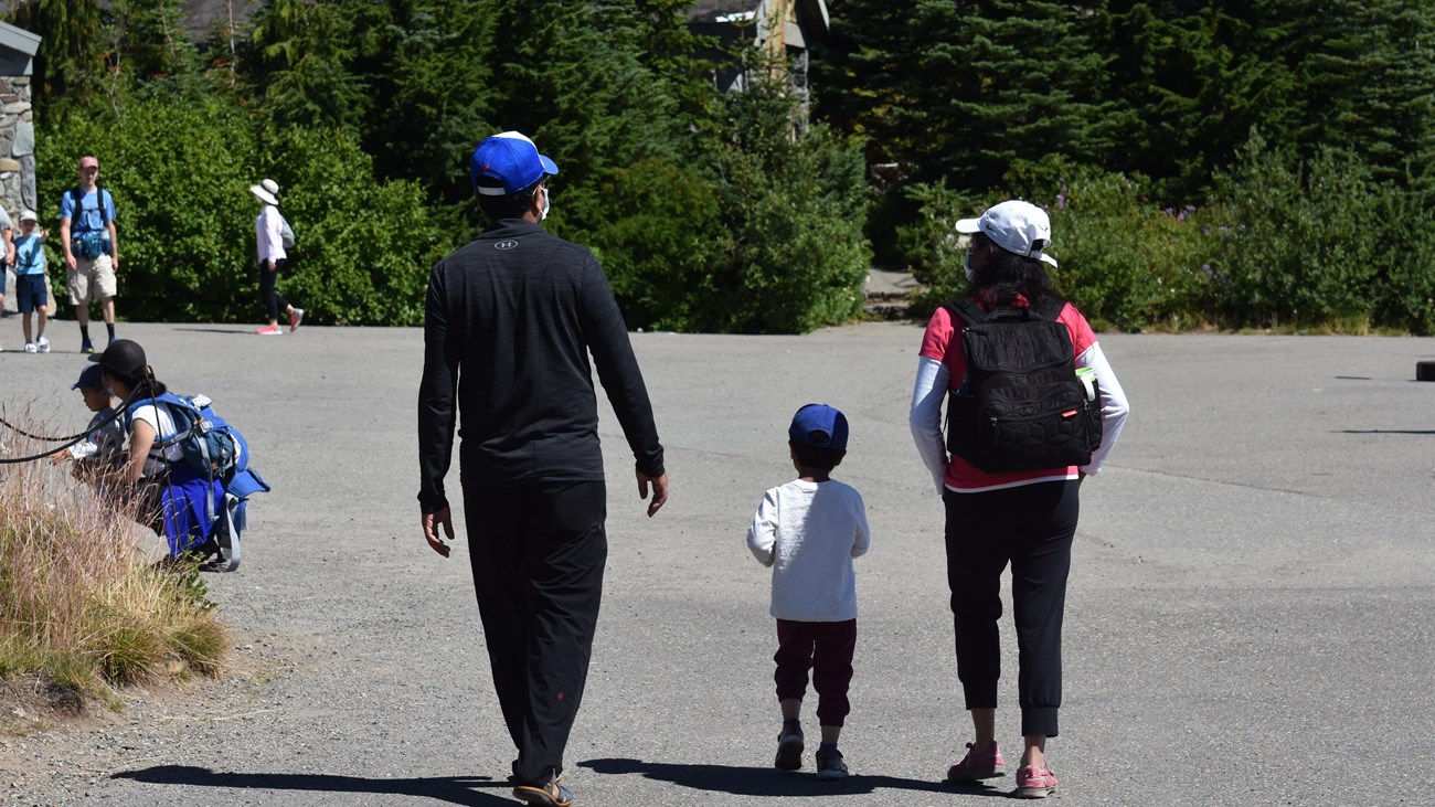 Two adults walking with a child between them on a paved pathway.