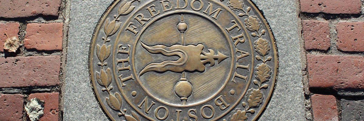 Bronze medallion with words The Freedom Trail Boston set in a red brick sidewalk.