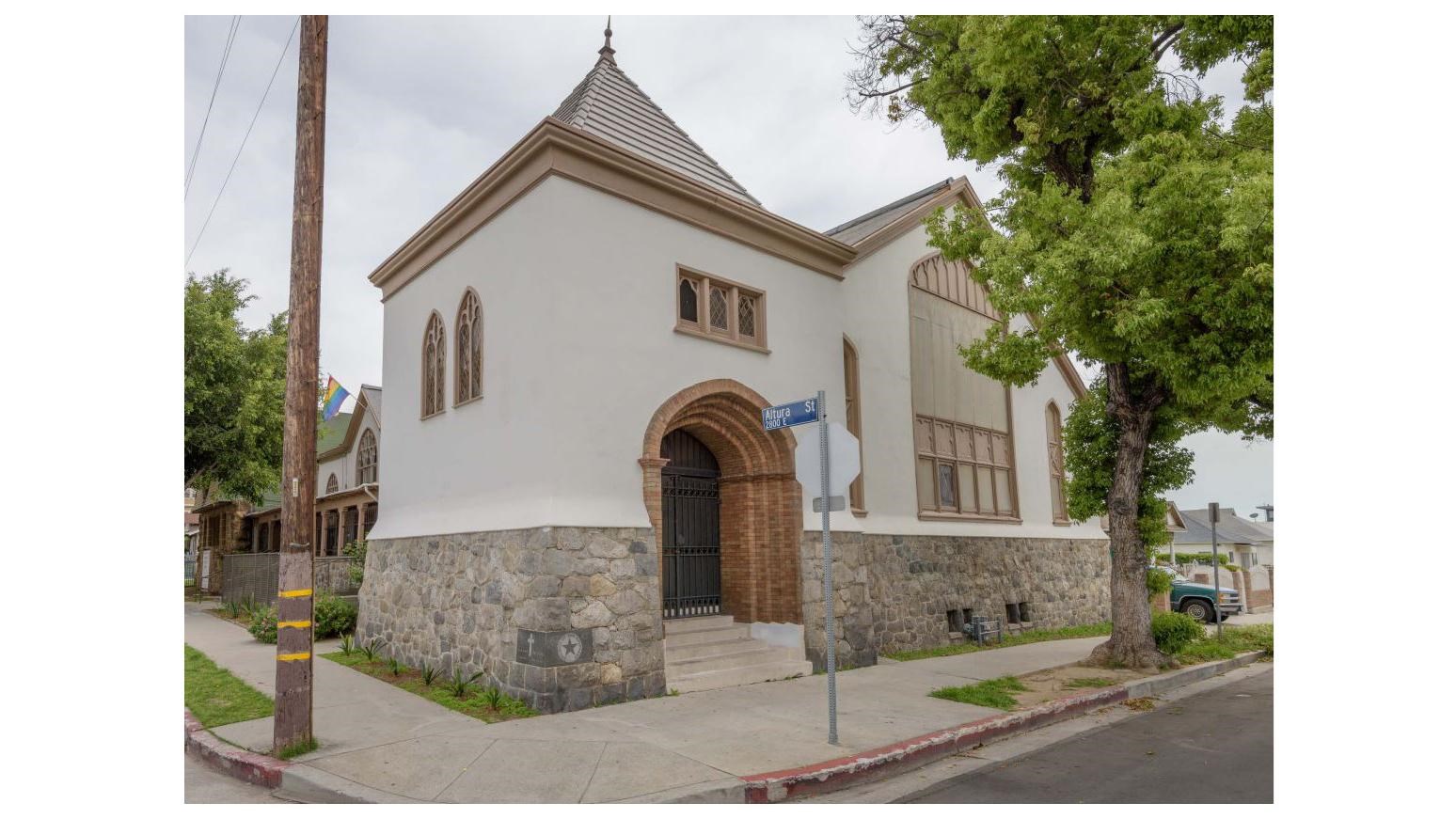 church building on the corner of an intersection with stone foundation a large metal arched door 