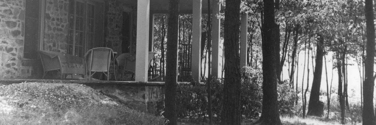 A stone house with large porch nestled among trees.