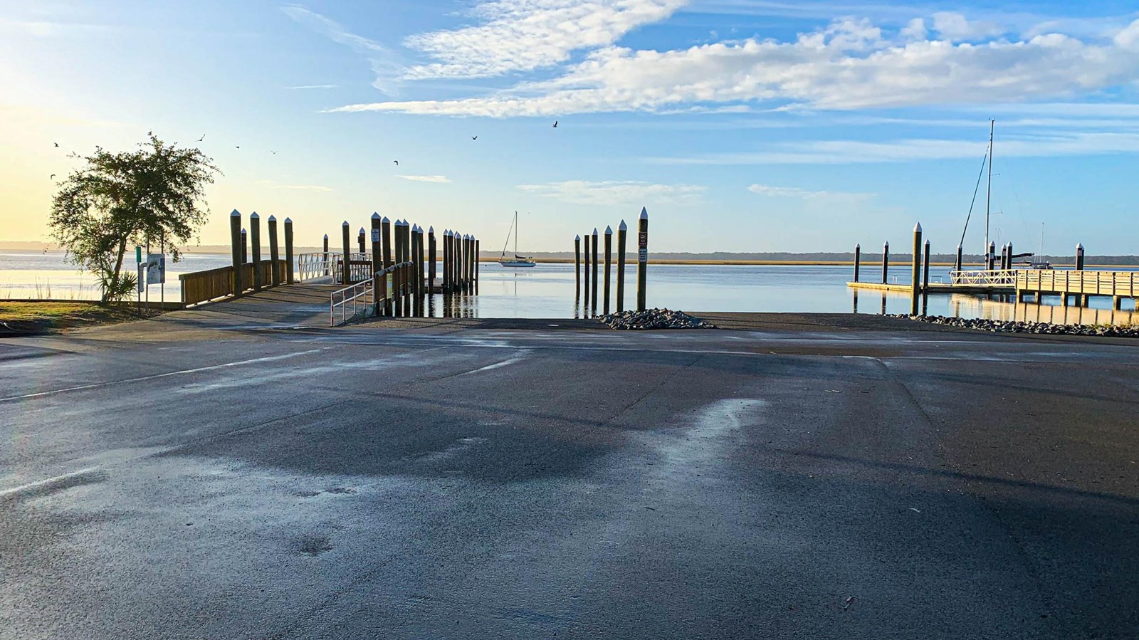 A large black top area leading to a concrete boat ramp with several floating docks.