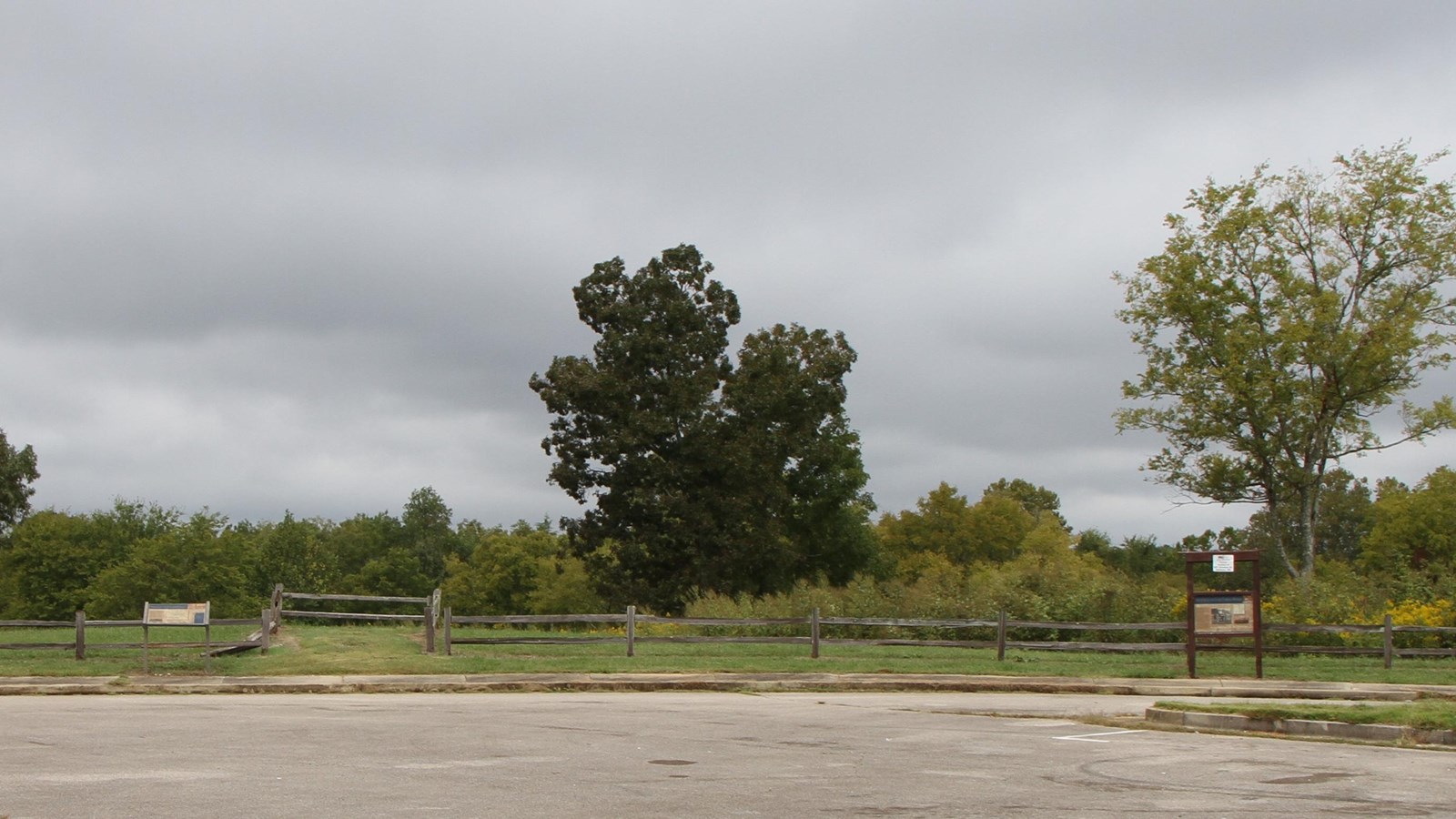 Large parkign area leads to two information panels. A wooden fence separates the site from the woods