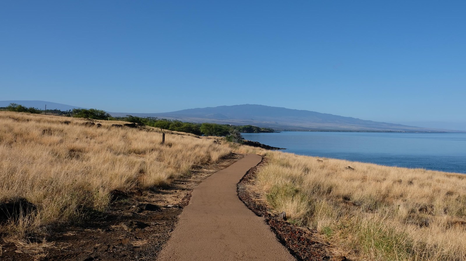Paved pathway by the sea with Hualalai volcano in the far distance